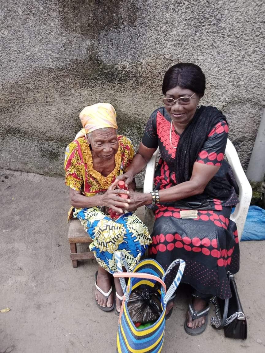 Une bénévole d'AMAPA AFRIQUE remet des médicaments et un panier de vivres à une femme âgée
